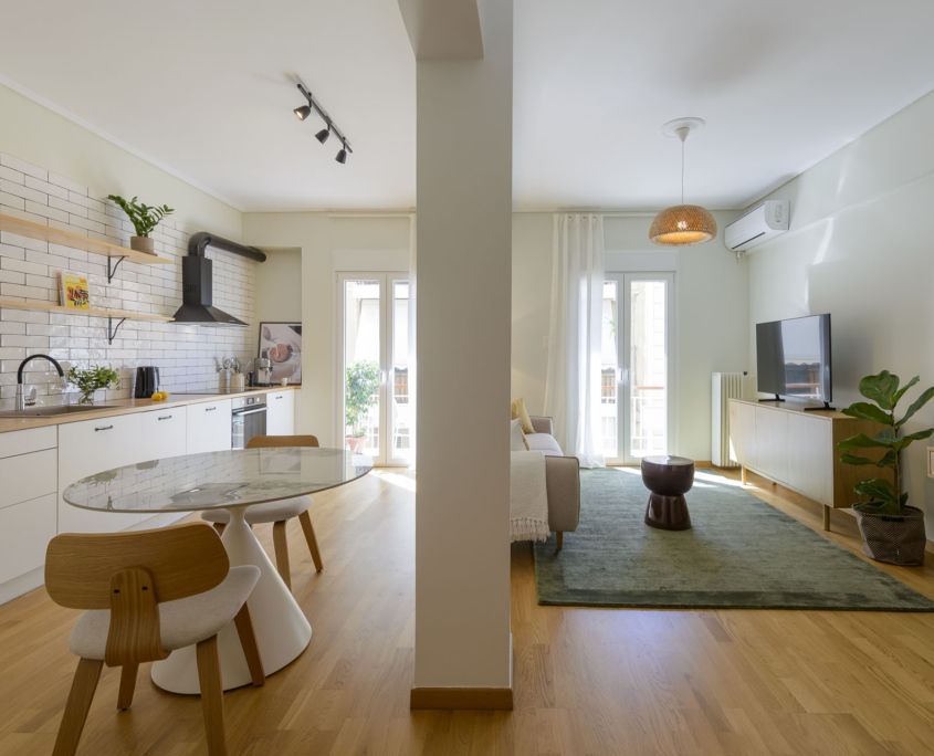 Open-plan living room and fully equipped kitchen with dining area and balcony access in furnished long stay apartment in Ano Petralona, Athens