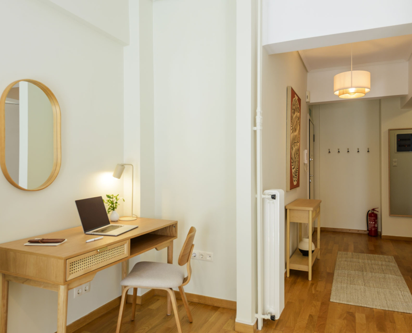 Dedicated workspace in the living area with view into entrance hallway and built-in storage in furnished long stay apartment in Ano Petralona, Athens