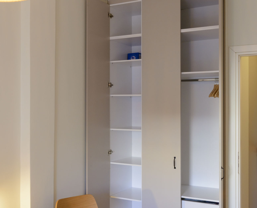 Open bedroom wardrobe with shelves and hanging rail in a fully furnished long stay apartment in Ano Petralona, Athens