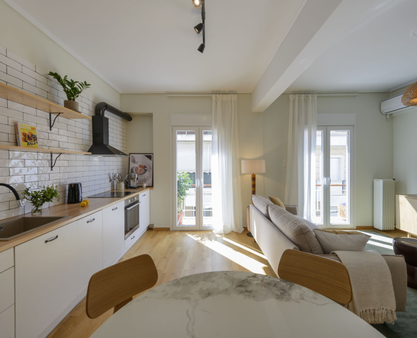 Open-plan living room and fully equipped kitchen with balcony access and natural light in furnished long stay apartment in Ano Petralona, Athens