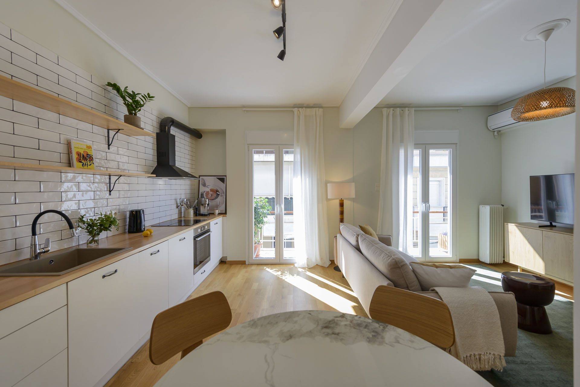 Open-plan living room and fully equipped kitchen with balcony access and natural light in furnished long stay apartment in Ano Petralona, Athens